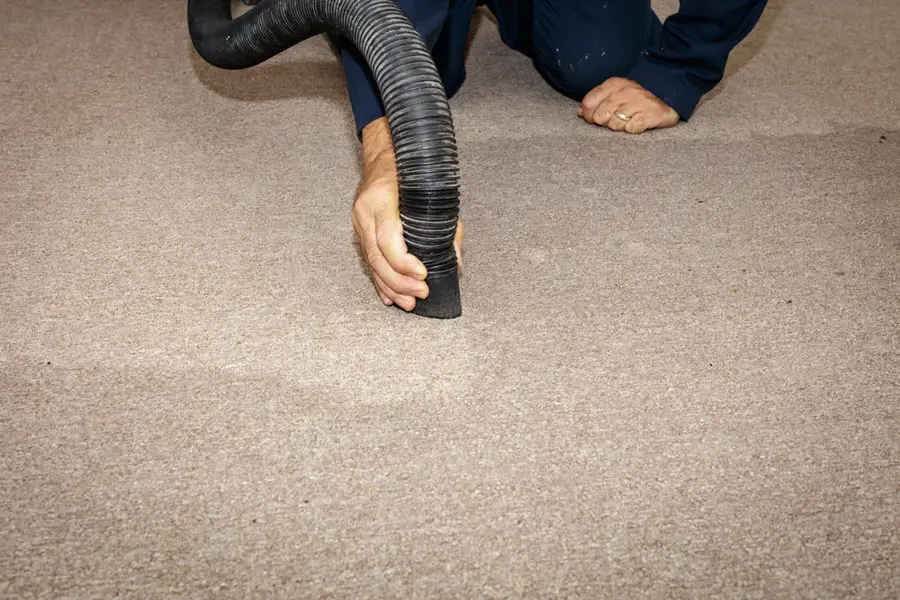 A hand guiding an extraction hose over wet carpet, the first hour of an Owasso water removal