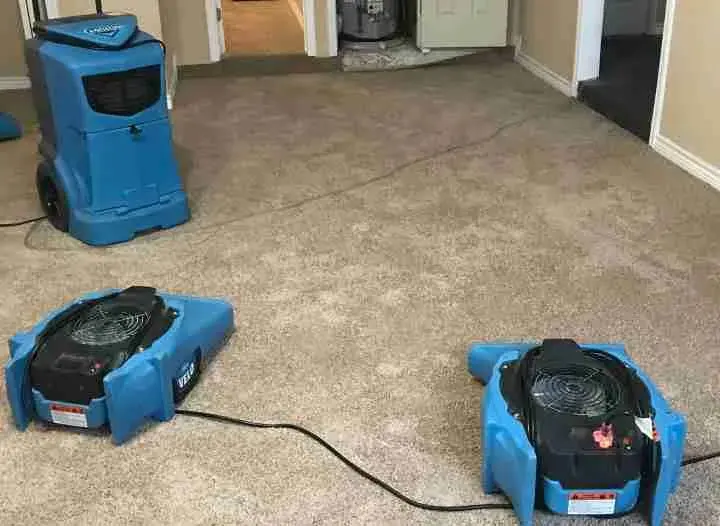 Blue air movers and a dehumidifier set on wet carpet, a standard setup for an Owasso dry-out