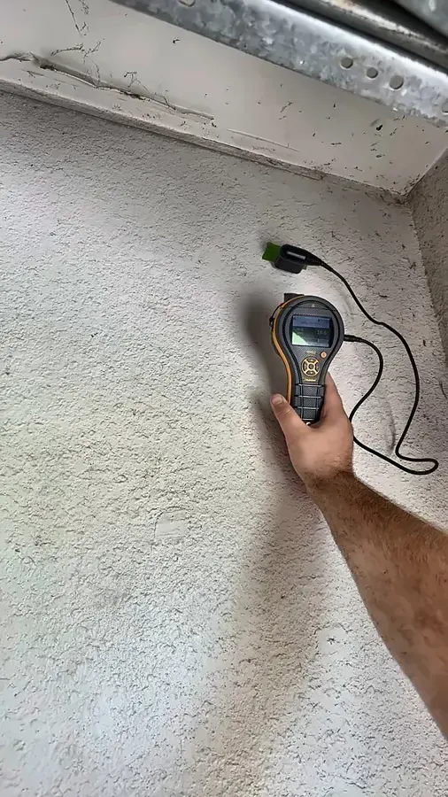 A pinless moisture meter held to a textured wall to find hidden water, an Owasso moisture check