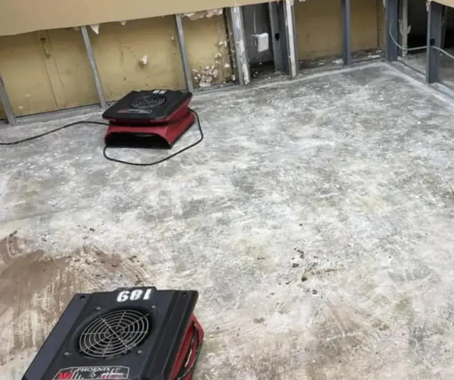 Red air movers on a bare concrete slab with the drywall cut away, slab drying in Owasso