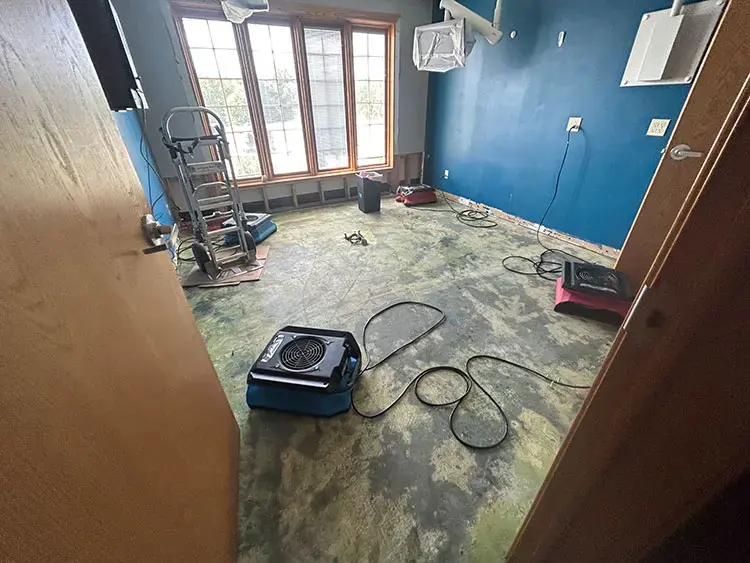 A small air mover and hoses on a water damaged floor in a room with blue walls during a dry-out in Claremore, Oklahoma.
