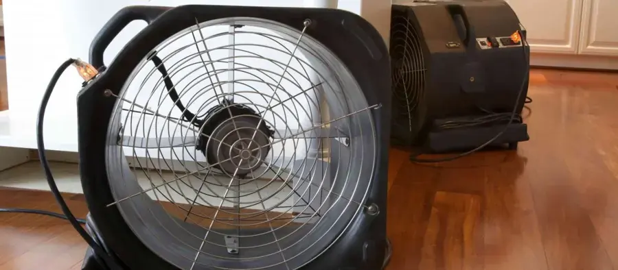 A black axial fan and a dehumidifier drying a hardwood floor, the kind of setup a Collinsville dry-out starts with after a leak