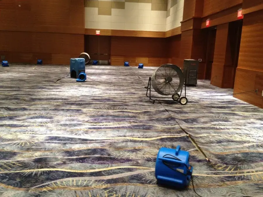 Air movers and a dehumidifier drying wet carpet in a large event hall, commercial water damage drying for Owasso businesses