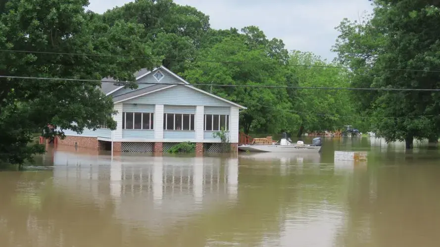 A house standing in brown floodwater after heavy rain, the kind of creek flooding that brings flood damage cleanup to Owasso