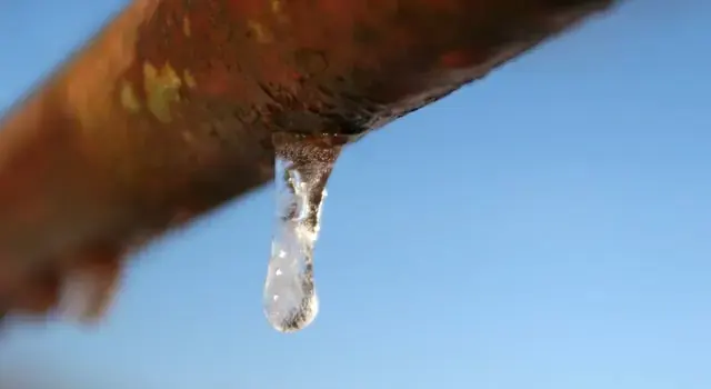 An icicle hanging from a rusted pipe in freezing weather, the kind of frozen pipe that bursts in an Owasso cold snap