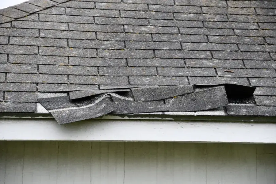 Wind-lifted and torn asphalt shingles at a roof edge, the opening behind many Owasso roof leaks