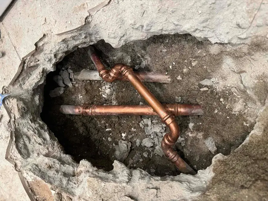 Copper supply pipes exposed through a hole in a concrete slab, the access a slab leak needs in Owasso homes