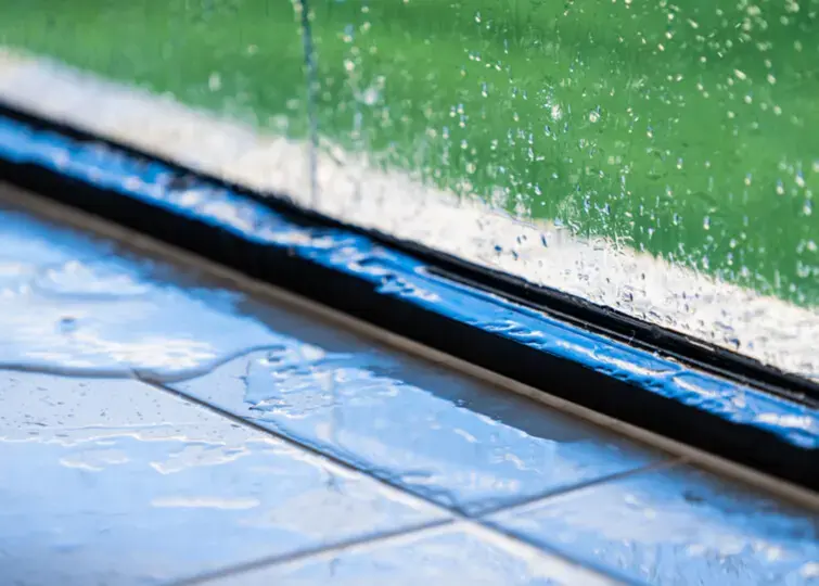 Storm rain beating on a window with water pooling in the frame, storm water damage for Owasso homes