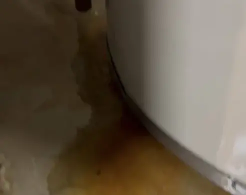 Rusty water spreading across the floor at the base of a leaking water heater tank, a water heater leak in Owasso
